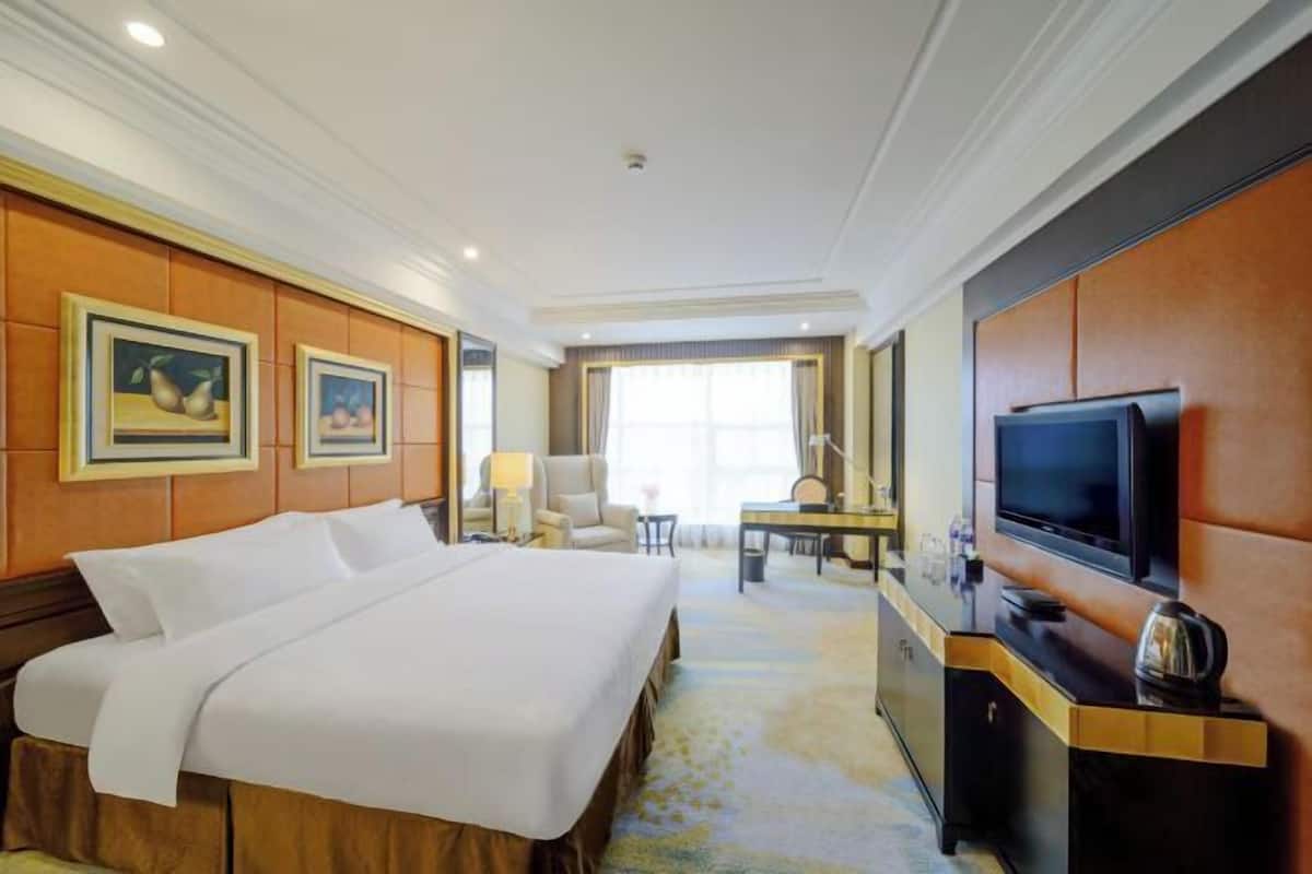 A hotel room with a large bed, a television, a desk with a chair, and framed artwork on the walls.