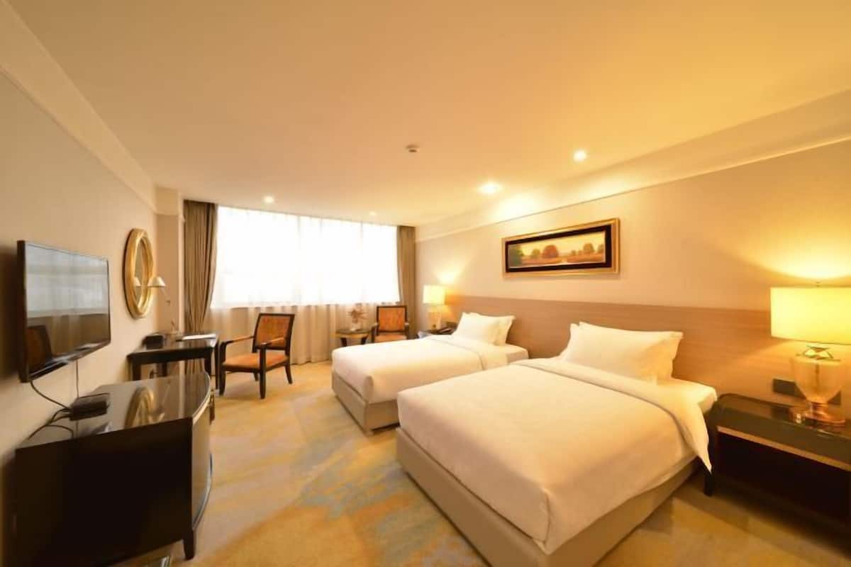 A hotel room with two beds, a desk, a TV, and a painting on the wall.