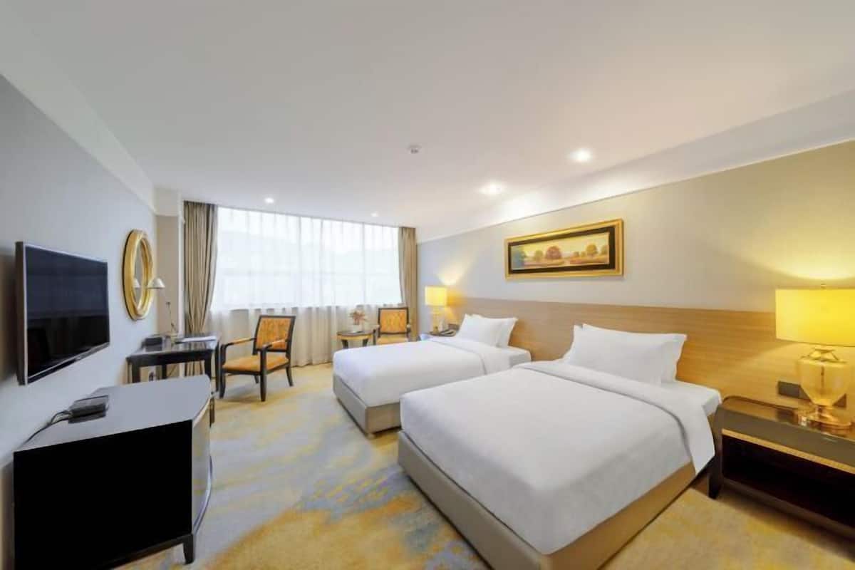 A hotel room with two beds, a desk with a TV, a chair, a lamp, and a painting on the wall.