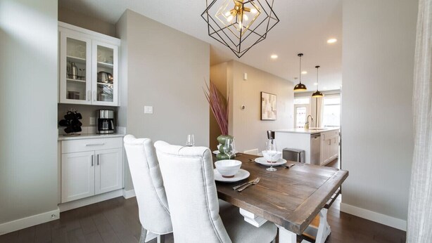 Un espace repas avec une table en bois, des chaises à revêtement blanc et un luminaire suspendu moderne.