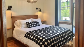A neatly made bed with a black and white polka dot bedspread, two bedside lamps, a wooden headboard, and a window with a view of greenery outside. - Retro-chic retreat in the heart of Wakefield (Wakefield)