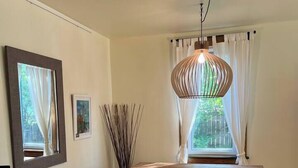 A room with a wooden table, a hanging light fixture, a framed picture, and a window with curtains. - Retro-chic retreat in the heart of Wakefield (Wakefield)