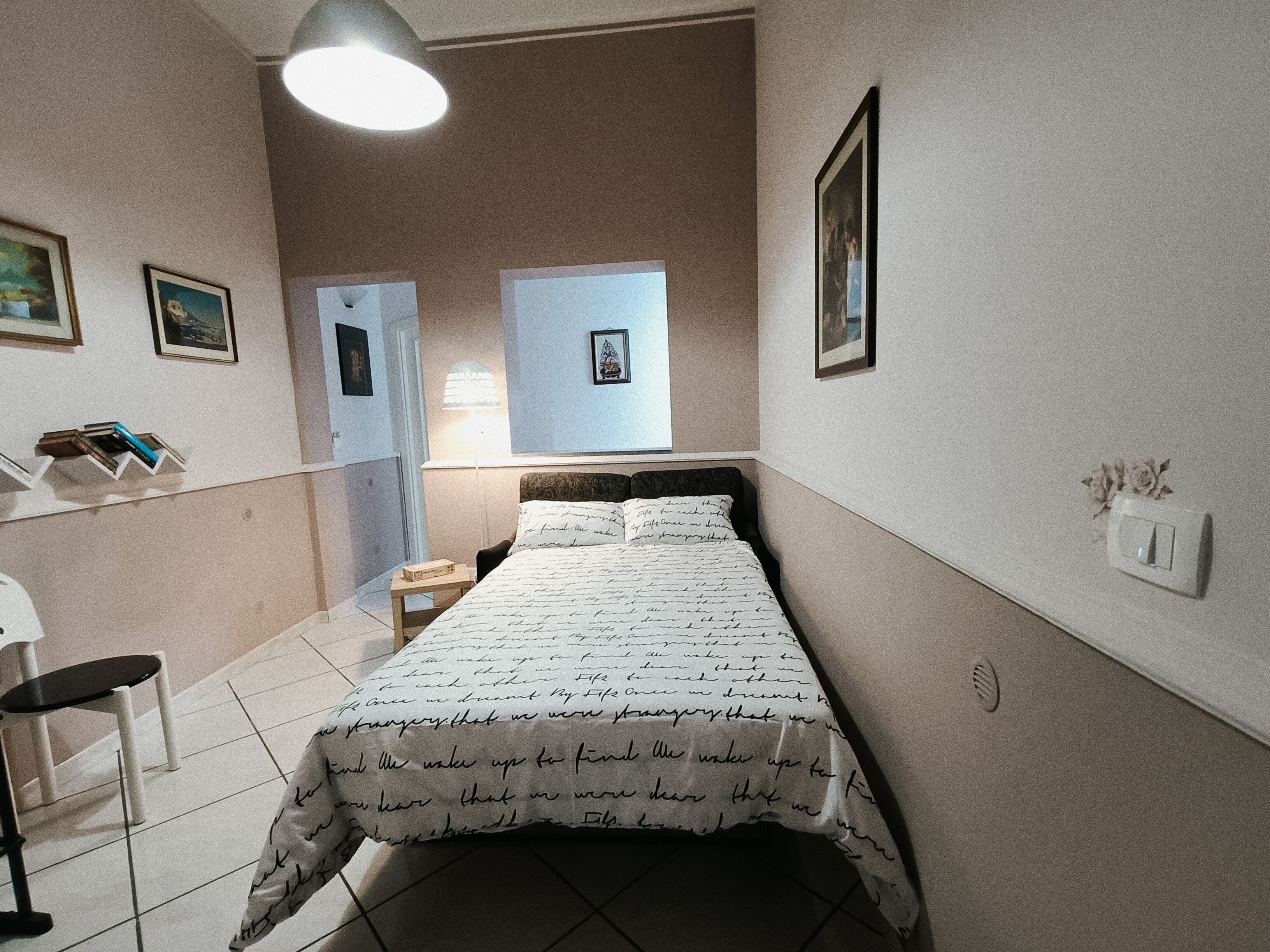 A bedroom with a bed, a bedside table, a chair, a lamp, and a wall-mounted light fixture.