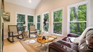 A spacious living room with large windows, a leather sofa, a rocking chair, and a coffee table with decorative items. - 3800 sq ft of Fun! Sleeps 14 • Hot Tub • Pool Table • PAC-Man • Foosball  (McGaheysville)