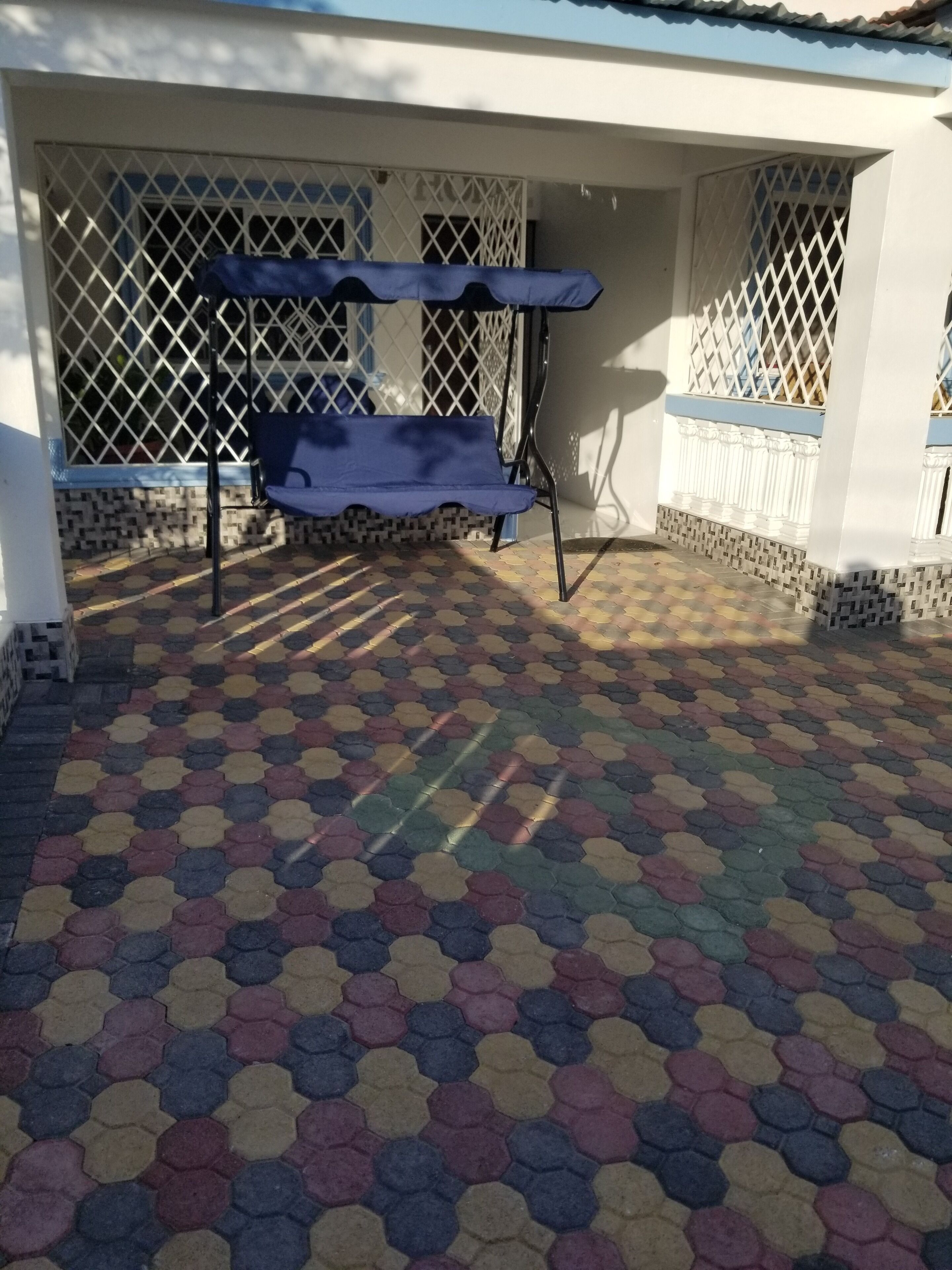 A covered outdoor area with a patterned floor, a bench, and a lattice window.