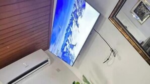 A room with a flat-screen TV mounted on the wall, a potted plant, a cushioned chair, and a dark wooden cabinet. - Cozy 2-bedroom stay with fireplace, AC, Wi-Fi and Comfort (Spanish Town)