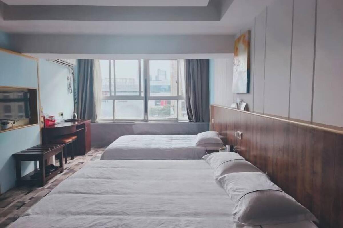 A hotel room with two beds, a desk, a chair, a mirror, and a window with curtains.