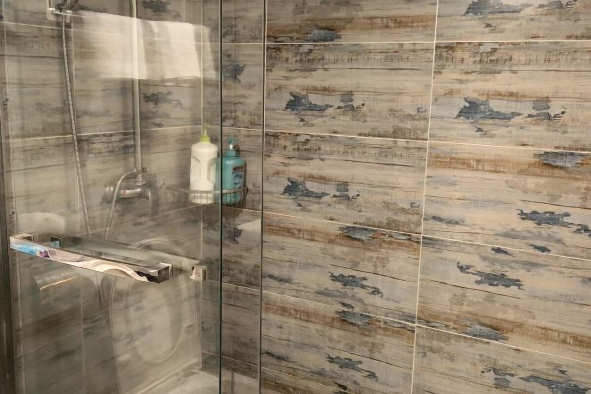 Une douche avec une porte en verre, un porte-serviettes et un distributeur de savon fixé au mur.
