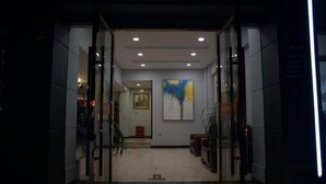 Un hall d’hôtel avec une entrée en verre, un tableau accroché au mur et un sol carrelé.