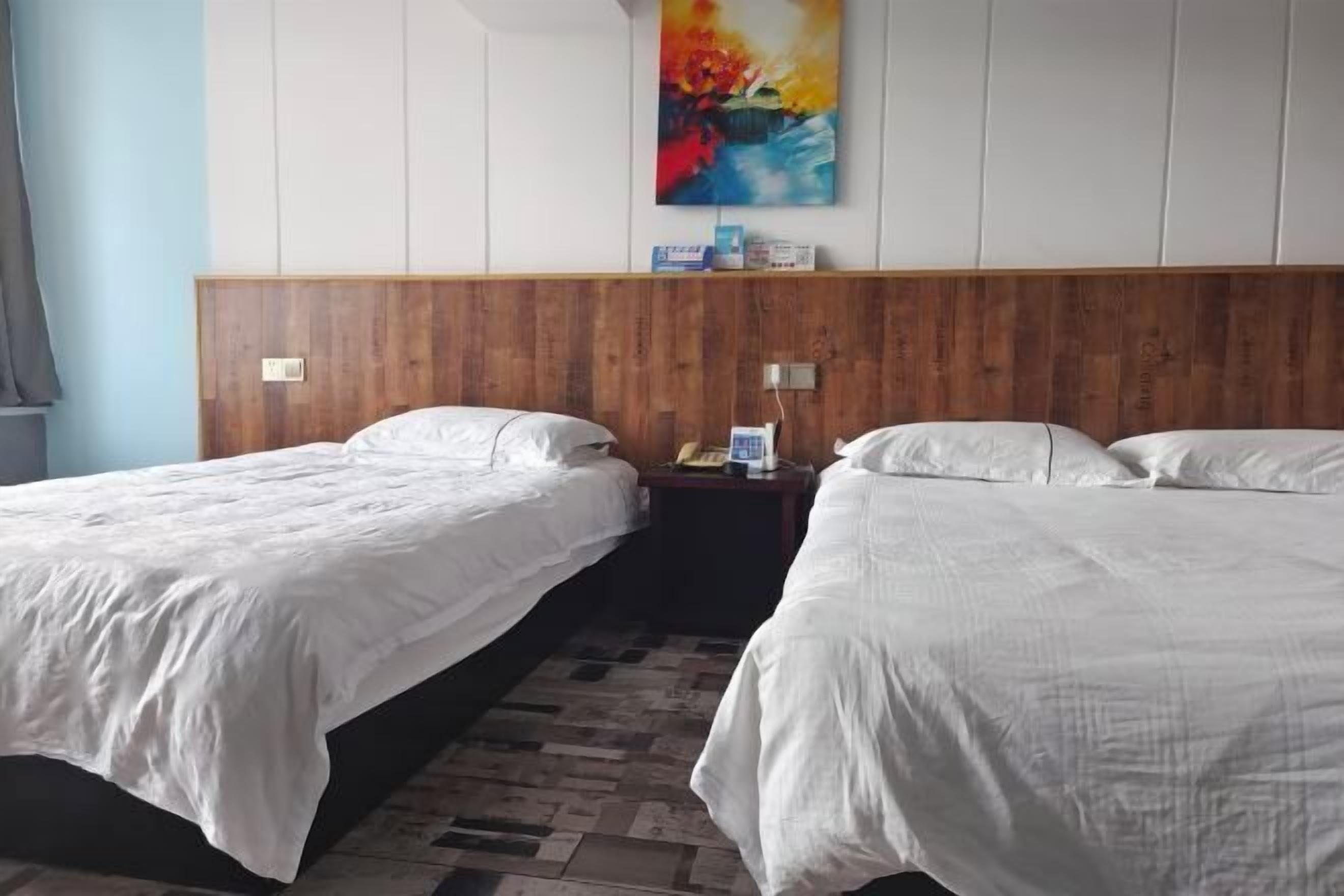 Una camera d'albergo con due letti singoli, una testiera in legno, un comodino con una lampada e un quadro appeso al muro.