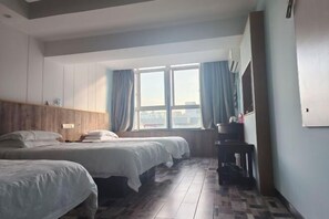 Une chambre d’hôtel avec deux lits, une tête de lit en bois, une fenêtre avec des rideaux, une petite table et un téléviseur fixé au mur.