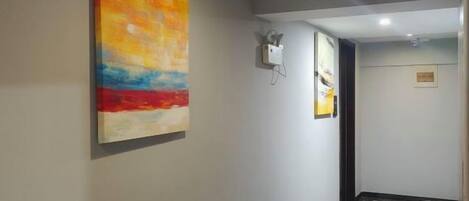 A hallway with a colorful abstract painting on the left wall, a light switch, and a door at the end.