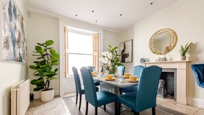 Ein Esszimmer mit Tisch für vier Personen, umgeben von Türkis-Stühlen, einem Kamin und einem großen Fenster.