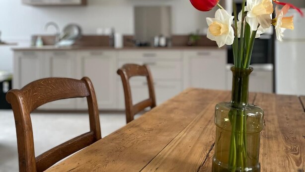 A wooden dining table with a vase of red and white flowers in the center. - Le Clos de Lignières : Chez Marguerite (Lignières-Châtelain)