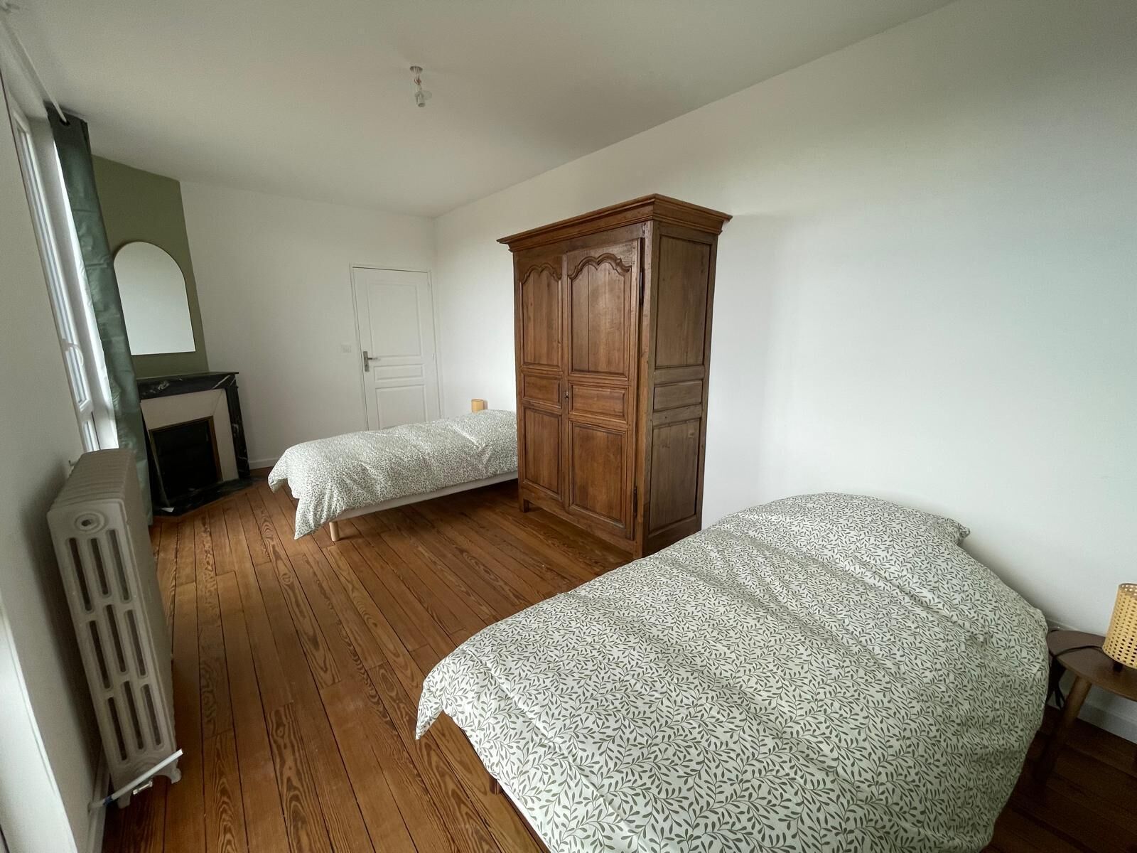 Een slaapkamer met twee eenpersoonsbedden, een houten garderobe, een radiator en een witte deur.