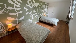 A room with two beds, a wooden floor, a green wall with white floral patterns, a door, and a window with curtains. - Le Clos de Lignières : Chez Marguerite (Lignières-Châtelain)