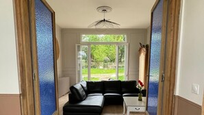 A modern living room with a black sectional sofa, a small white table, and a large window offering a view of a garden. - Le Clos de Lignières : Chez Marguerite (Lignières-Châtelain)
