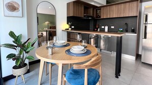A modern kitchen with wooden cabinets, a stainless steel refrigerator, and a dining area with a round table and blue upholstered chairs. - Parque el Virrey modern & luxury apartment (Bogotá)