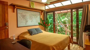 Une chambre à coucher avec un lit, une carte accrochée au mur, une fenêtre donnant sur un paysage verdoyant et un ventilateur de plafond.
