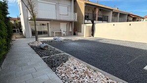 Un quartier résidentiel avec un trottoir dallé, un petit arbre et un immeuble doté d’un balcon.