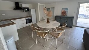 Une cuisine moderne avec des meubles blancs, une table à manger ronde entourée de chaises en osier et un meuble gris.