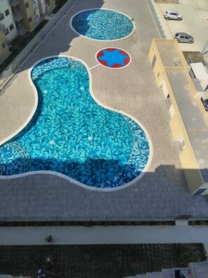Vista aérea de un complejo de piscinas con varias albercas y un diseño en forma de estrella en el suelo.