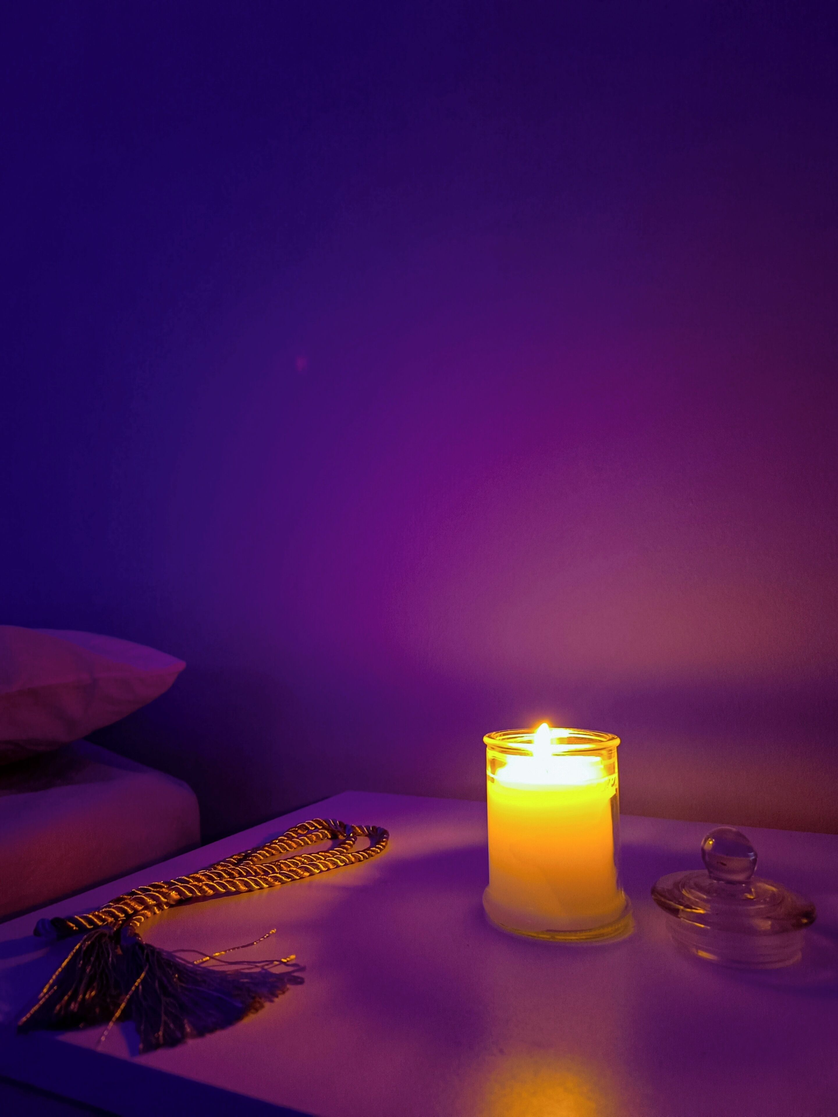 A candle on a table with a decorative item and a glass container.