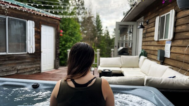A person sitting in a hot tub with a wooden house and a white couch in the background. - CDA Lake-Kayaks-Hot Tub-Boat Slip & More! (Worley)