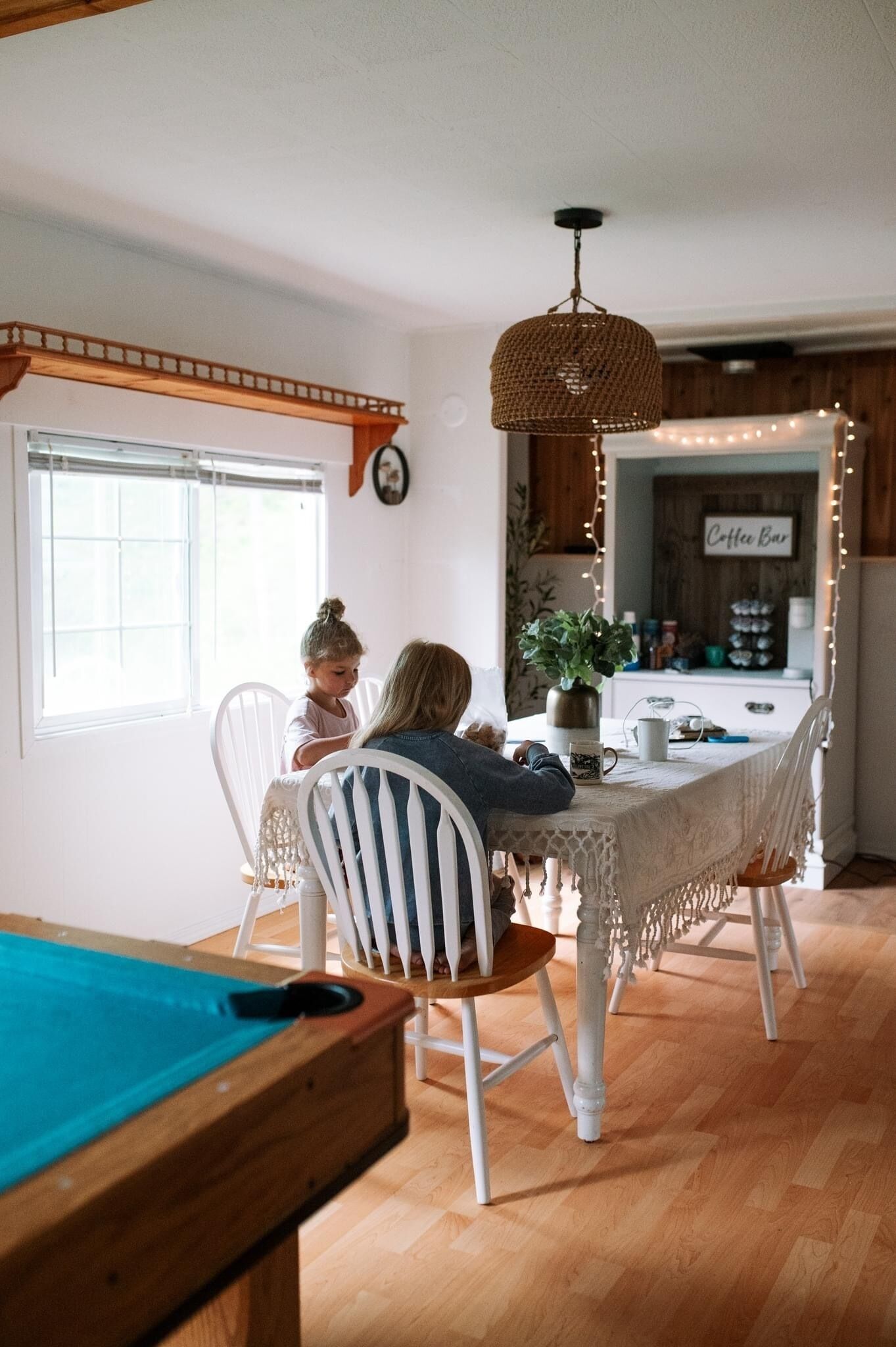 A dining area with a pool table, white chairs, and a kitchen in the background.