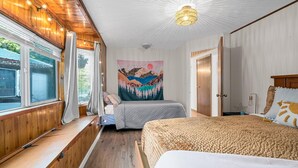 A bedroom with two beds, wooden paneling, a large window, and a ceiling light fixture. - CDA Lake-Kayaks-Hot Tub-Boat Slip & More! (Worley)