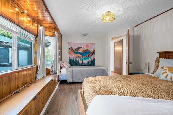 A bedroom with two beds, wooden paneling, a large window, and a ceiling light fixture.
