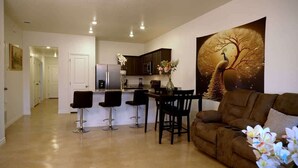 A modern kitchen with dark cabinets, a dining area with a table and chairs, and a large wall painting of a tree and peacock. - Peaceful Stay Near Fort Cavazos (Copperas Cove)