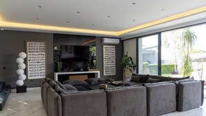 A modern living room with a sectional sofa, a flat-screen TV, and a large window offering a view of the outdoors. - Luxurious Country Home in Zapopan by Magnolia Homes (Zapopan)