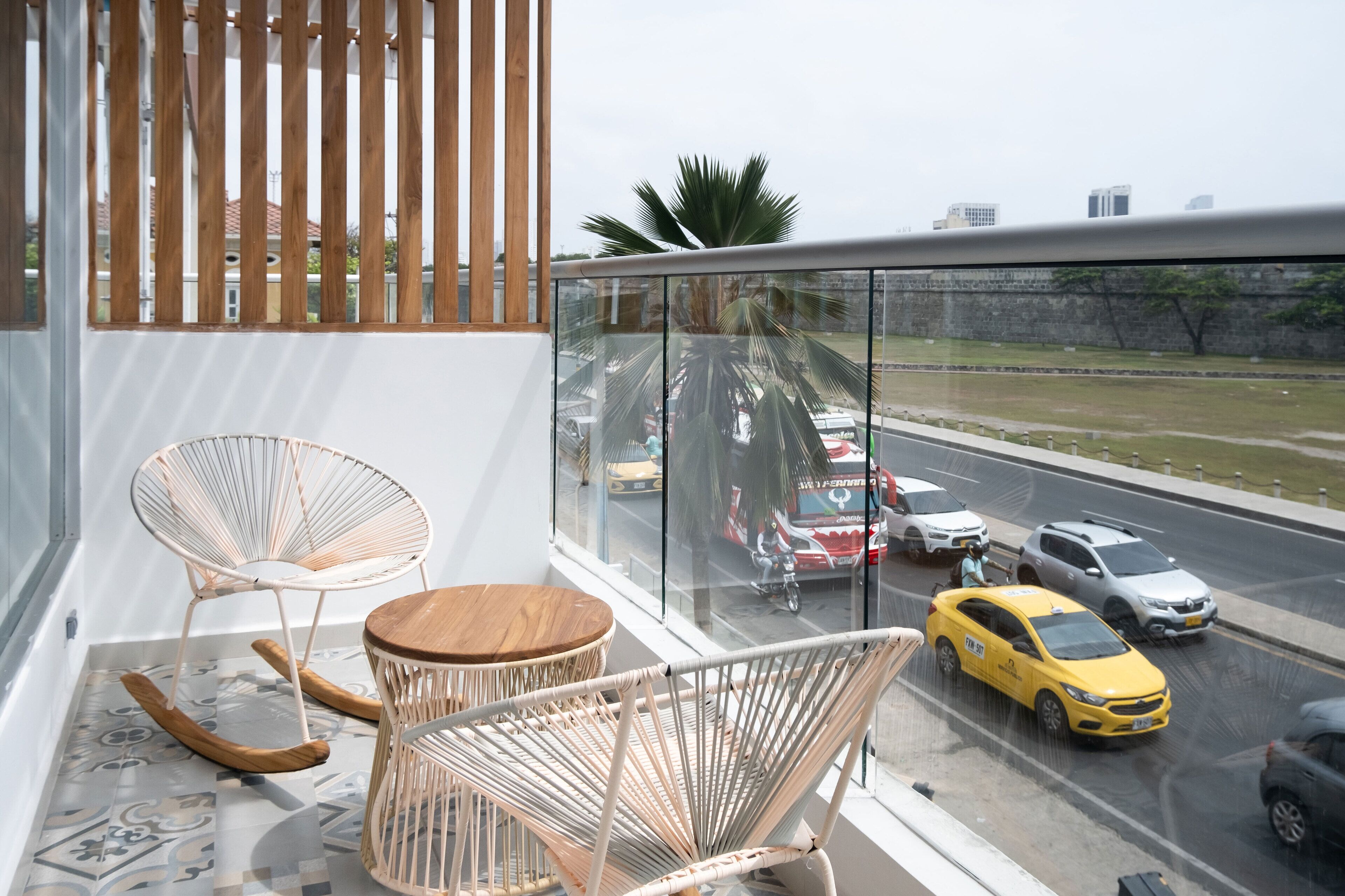 Ein Balkon mit Korbmöbeln, Blick auf eine belebte Straße und eine Stadtkulisse im Hintergrund.