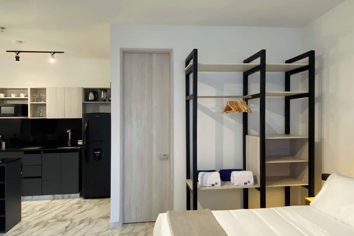 Una habitación de hotel compacta con cama, armario, pequeña cocina y una puerta que da a otra habitación.