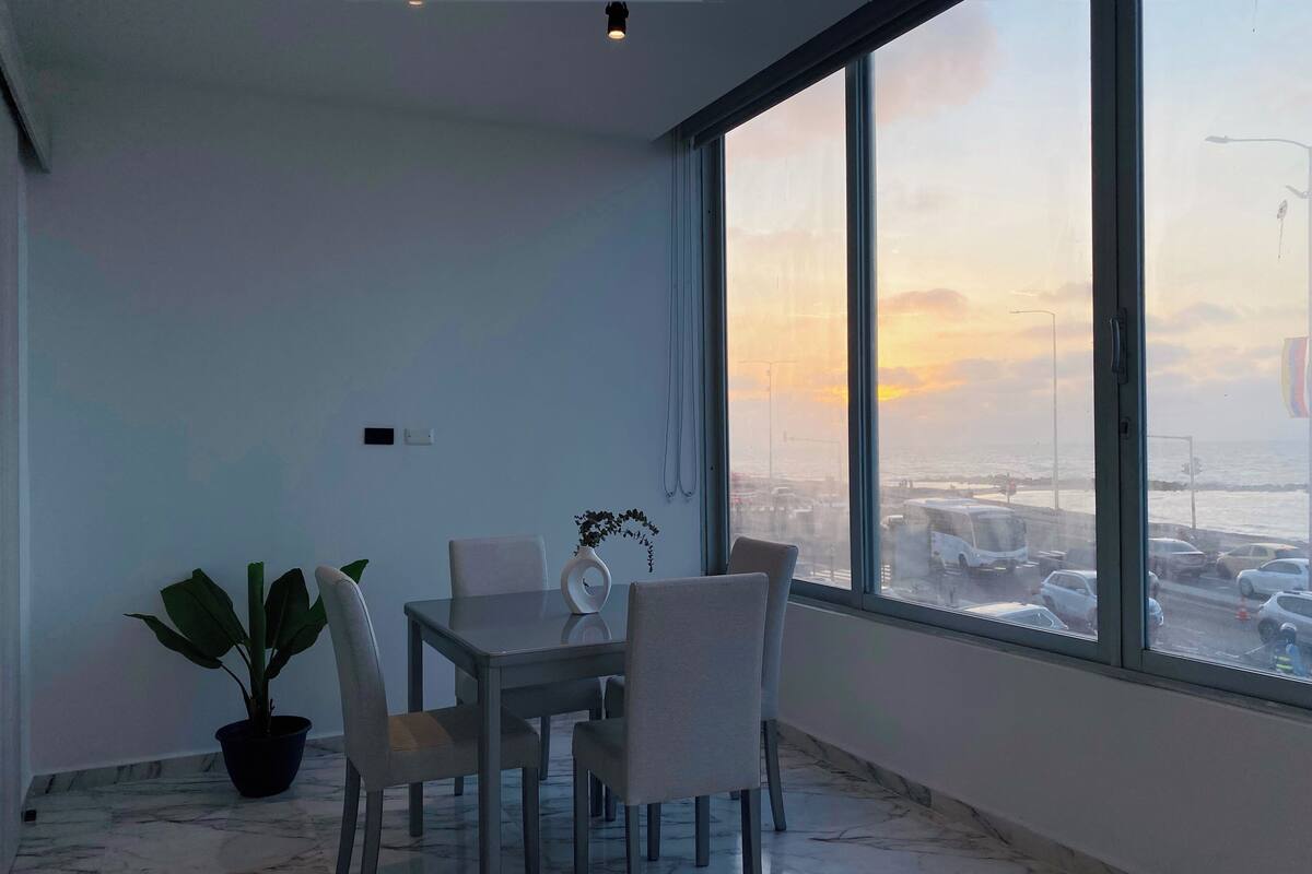 Un comedor moderno con un gran ventanal, una planta en maceta y un suelo de mármol.