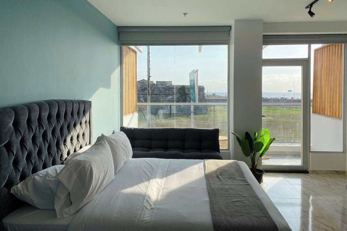 Un dormitorio con una cama grande, vista al mar y un balcón con una planta.