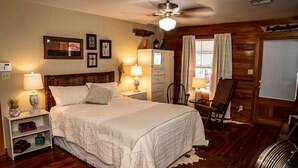 A bedroom with a large bed, wooden walls, a ceiling fan, and a window with curtains. - Charming 2-bedroom house in fabulous Breaux Bridge with WiFi, AC (Breaux Bridge)
