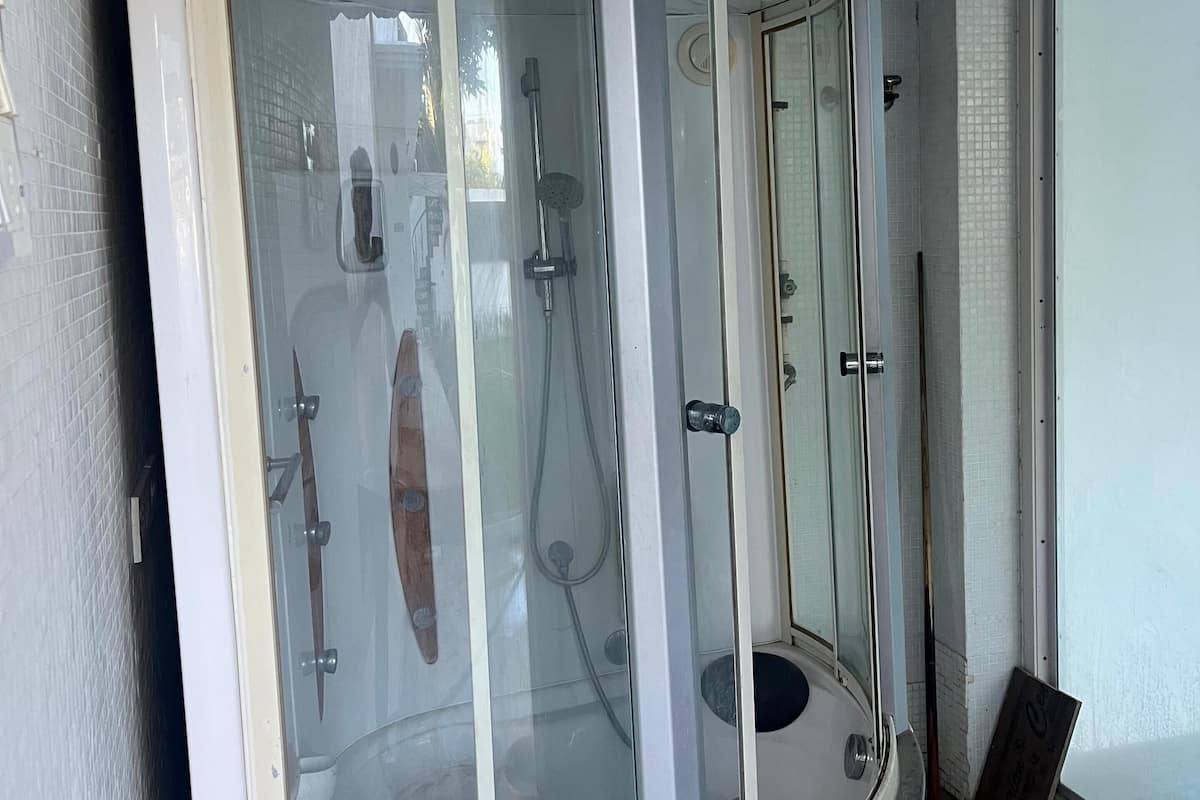 A glass-enclosed shower area with a curved design, a visible showerhead, and a door with a handle.