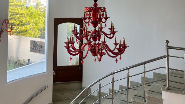 Uma escadaria imponente com um lustre vermelho, vista para o exterior e piso de mármore.