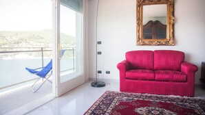 A room with a red sofa, a patterned rug, a large mirror, and a view of a body of water through a sliding door.