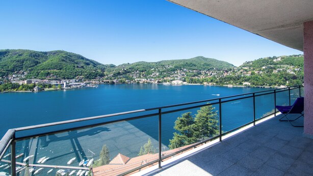 A balcony with a clear view of a lake, boats, and a town across the water.