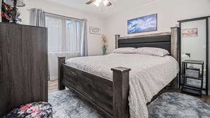 A bedroom with a bed, a ceiling fan, a nightstand, a lamp, and a window with curtains.
