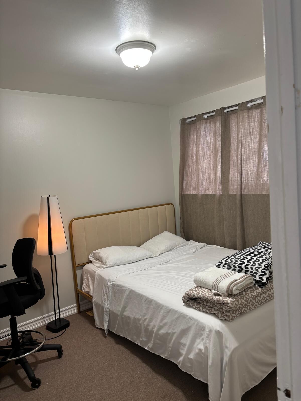 A bedroom with a bed, a desk, a chair, a lamp, and a ceiling light.