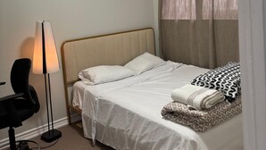 Une chambre à coucher comprenant un lit, un bureau, une chaise, une lampe et un luminaire au plafond.