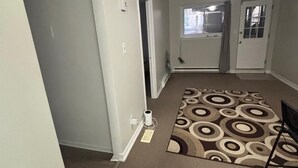 Un couloir avec un tapis à motifs, des murs blancs et une porte donnant sur une autre pièce.