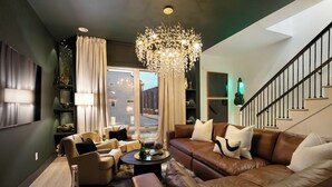 A modern living room with a brown leather sofa, beige armchairs, and a chandelier.