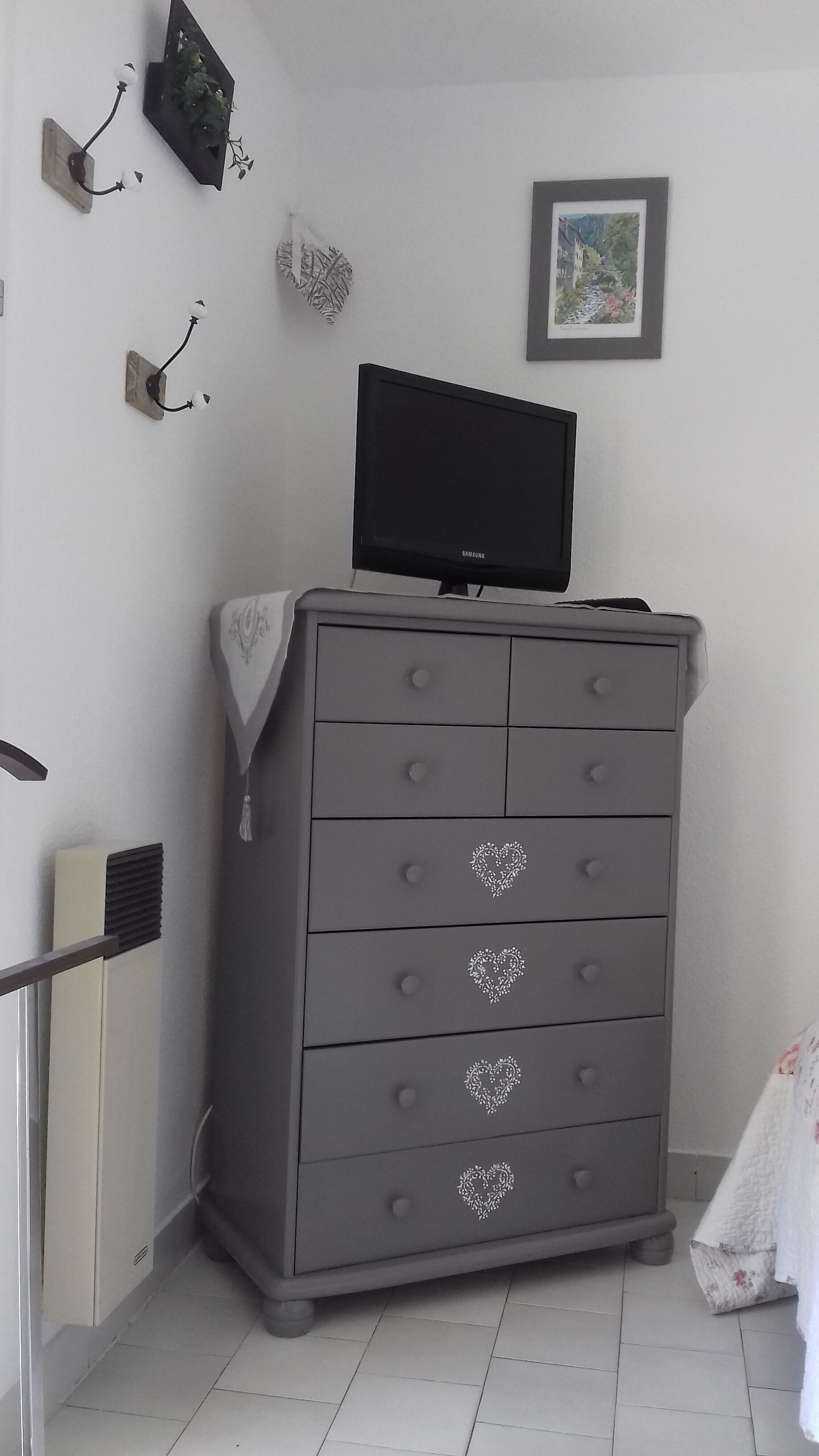 A grey dresser with a flat-screen TV on top, a decorative wall piece, and a framed picture.