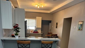 Een moderne keuken met een marmeren vloer, twee barkrukken, een centraal eiland en een eetgedeelte met tafel en stoelen.