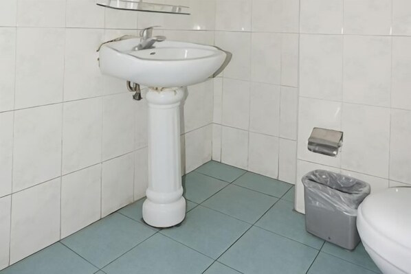 Une salle de bain avec un lavabo sur colonne, des toilettes et une poubelle.